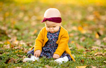 A little girl 1 year old dressed in a yellow shirt and a white hat sits in a grey stroller in the park.