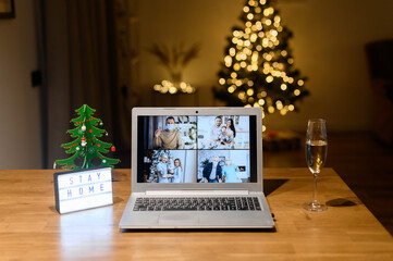 A laptop on the table with a several families on the screen in cozy living room decorated to Christmas. Virtual meeting, video call, online celebration with a family on the distance due to pandemic