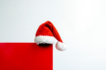 Minimal Christmas composition. Red cube shape podium with Santa Claus hat on white background with copy space.
