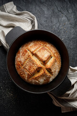 Traditional sourdough bread baked in a dutch oven on a black background top view