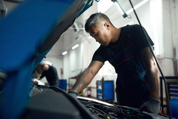 Young asian mechanic working with engine near open hood