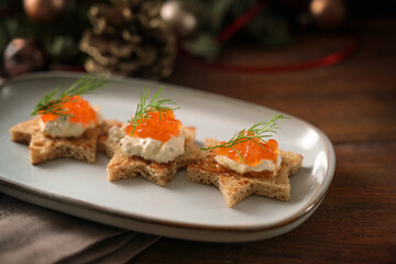 Canapes with red caviar, cream and dill garnish on toasted bread in star shape on a gray plate, dark rustic wooden table with holiday decoration, selected focus