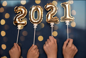 2021 the numbers on the inflated gold balls with bokeh from the lights of the garland hold their hands up. The concept of new year and Christmas.