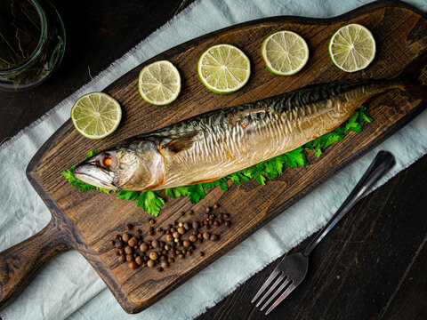 Appetizing cold smoked mackerel with ingredients on a cutting board. On dark wooden background