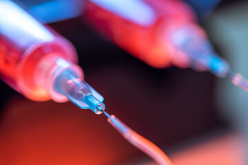 Pump pushing red liquid medium through syringes and flexible tubes in a small chip devise for an experiment in a scientific laboratory.