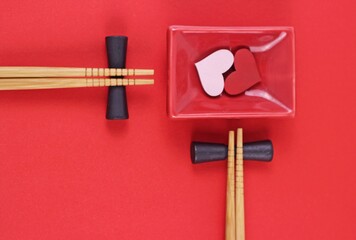 Two couples of wood chopsticks and ceramic saucer with hearts on red table.Sushi rolls asian restaurant holiday menu background.Valentine's Wedding Day concept.Top view with place for text.