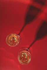 Two glasses of champagne on a red background with hard shadows. Holiday and New Year concept. Top view, copy space 