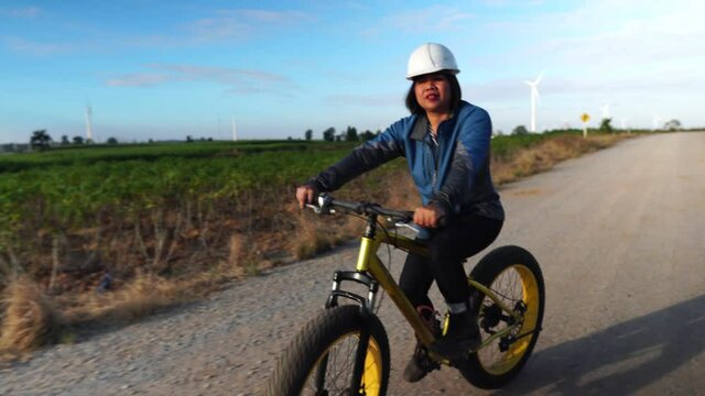 Footage 4K: A female Asian engineer is riding a bike to inspect wind turbine systems