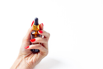 Woman hand with red manicure, small bottle with natural oil or cosmetic in hand.