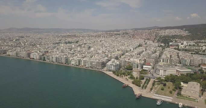 Aerial drone view of iconic historic landmark - old byzantine White Tower of Thessaloniki or Salonica with traditional tourist boats travelling Thermaikos gulf, North Greece