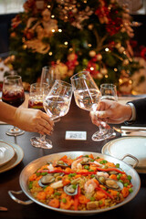 People sharing Spanish dinner table with assortment of dishes. paella, octopus, whole fish, sangría and wine. Dressed for christmas