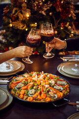 People sharing Spanish dinner table with assortment of dishes. paella, octopus, whole fish, sangría and wine. Dressed for christmas