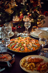 Spanish dinner table with assortment of dishes. paella, octopus, whole fish, sangría and wine. Dressed for christmas