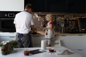 Young father and his small pretty daughter making Christmas lollypops together. Kitchen is decorated for New Year.