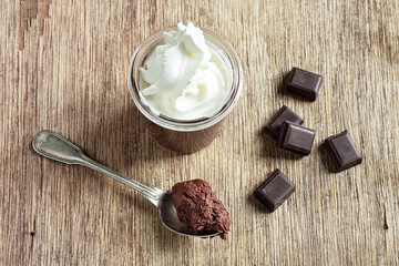 A glass and a teaspoon with chocolate mousse and pieces of dark chocolate on the old table, top view
