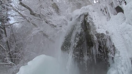 A small forest waterfall in the winter forest falls from a cliff. It is very cold, the water soars, ice freezes on the ledges. - Powered by Adobe