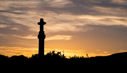 silhouette of stone cross backlit at sunset