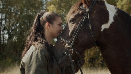 A charming young woman expresses her gratitude to a horse for a pleasant ride on it by hugging, kissing and stroking it.