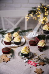 Chocolate and cherry cupcakes with mascarpone frosting and gingerbread cookies on festive table with bokeh lights on background.