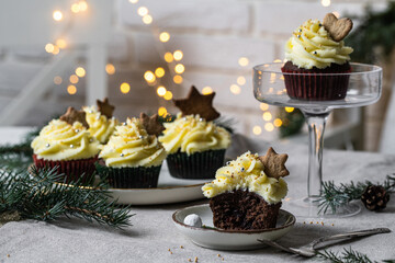 Chocolate and cherry cupcakes with mascarpone frosting and gingerbread cookies on festive table with bokeh lights on background.
