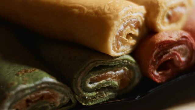 Thin tasty colorful pancakes. Macro view of red, yellow and green cutaway rolled pancakes with cream cheese and salmon filling on a dish. 4K video. Slowmotion
