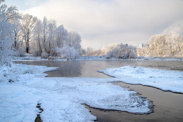 Winter day on the river, partially covered with ice. On the shore there are trees in hoarfrost.