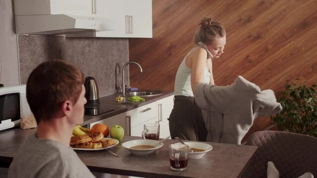 While the husband calmly drinks tea in the morning, the wife is late for work, she talks on the phone and quickly changes clothes