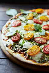 Pizza with cherry tomatoes, mozzarella and basil pesto. Dark wooden background. Close up. 