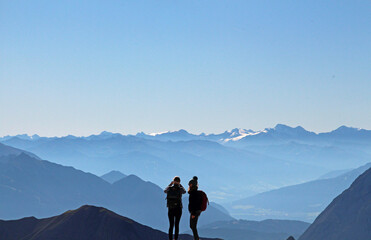 Zwei Personen im Vordergrund vor Berg Panorama in den Alpen bei blauem Himmel und Sonne