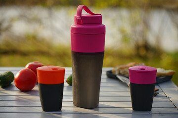 A set of camping utensils stands on a folding table in nature. Tourist liquid containers