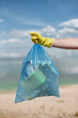 Volunteer or eco activist wearing yellow rubber gloves holding trash bag with plastic waste and...