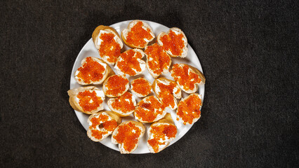 Top view of sandwiches with red caviar and butter on baguette on the dark background. Cuisine concept.