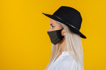 Woman wearing stylish protective face mask and black cap, posing on yellow background. Trendy Fashion accessory during quarantine of coronavirus pandemic. Close up studio portrait