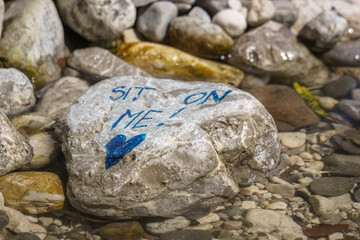 Stone in river with letters telling sit on me