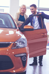 Dealer with woman stands near a new car in the showroom
