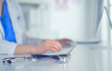 Close-up of stethoscope is lying on the table near female doctor typing on laptop computer