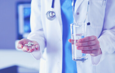 shot of doctor's hands holding pills and glass of water at clinic.