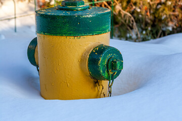 Yellow Fire hydrant with green cover and bolts partly buried in snow after a heavy winter snowfall...