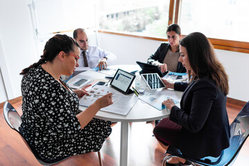 business meeting 4 people with laptops ipad tablet folios pens and folios in bright office with...