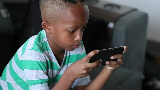 African boy touching face while playing video-game on smartphone device
