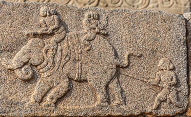 Hampi, Karnataka, India - November 4, 2013: Mural sculpture on stone at Royal Enclosure. Closeup of mural gray sculpture of elephant with several people on top and one poking it with stick.