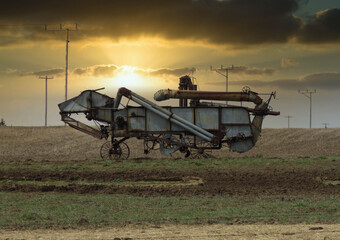 Fototapeta premium A horizontal photo of a old vintage thrashing machine standing in the field with a beautiful sunset.