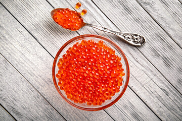 Fresh salted red salmon caviar with a silver spoon with eggs of ideal spherical shape in a transparent bowl. Premium quality product.