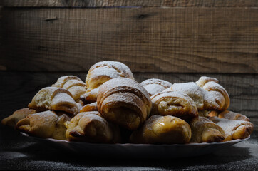 Homemade cookies in the form of bagels with jam filling sprinkled with powdered sugar on a wooden background.
