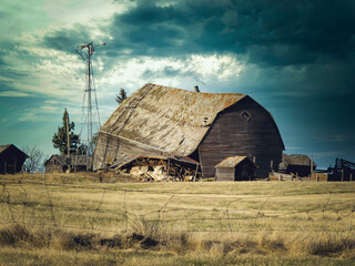 A horizontal photo of a old falling barn in the countryside with some dark clouds. © Marge