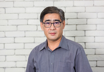 Portrait of Asian handsome senior elderly man wear eyeglasses on white brick wall background. Old...
