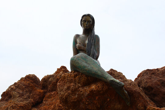 Mermaid statue made of bronze. The background is cloudy in white color.