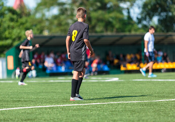 Boys in black sportswear plays football on field, dribbles ball. Young soccer players with ball on green grass. Training, football, active lifestyle for kids
