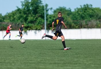 Obraz premium Boys in black sportswear plays football on field, dribbles ball. Young soccer players with ball on green grass. Training, football, active lifestyle for kids