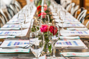 A long table set up for Christmas dinner with placemats, cutlery, glasses and flowers